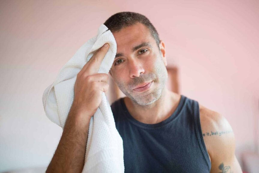 A man wipes sweat with a towel indoors, showcasing post-exercise relaxation. mental health medications excessive sweating