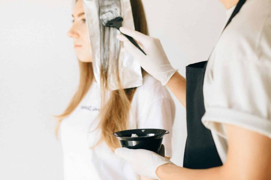 Hairdresser applying color to woman's hair in salon using brush and foil technique.