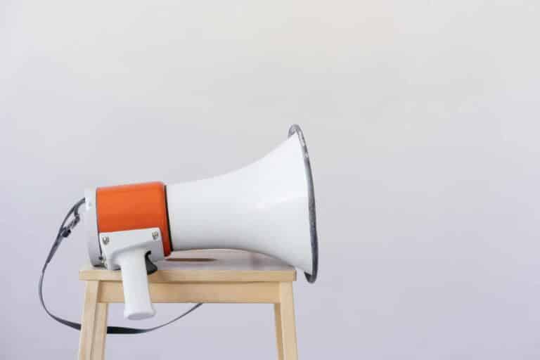 outspoken, Close-up of a megaphone resting on a wooden chair with a minimalist background.
