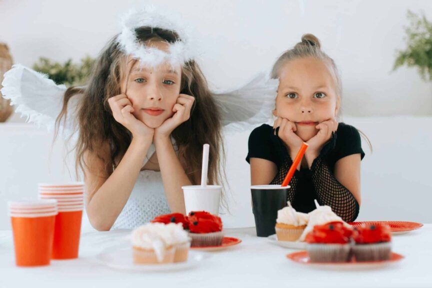 Two young girls dressed as an angel and demon at a Halloween party with cupcakes. fall drinks for kids, kids drinks,