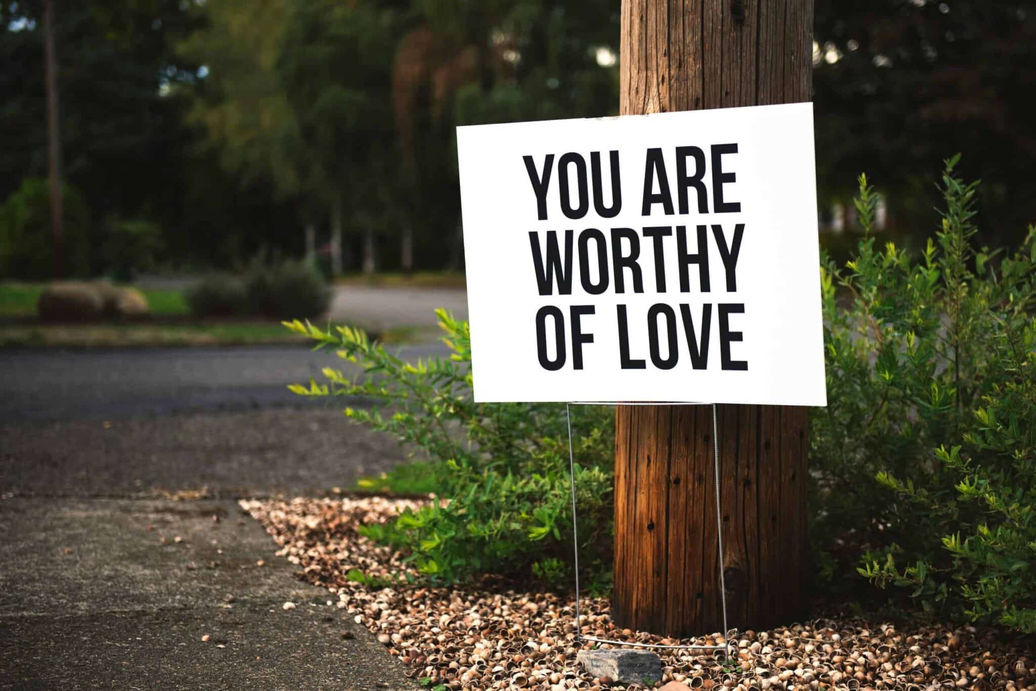 A positive message sign "You are worthy of love" in a park setting. self-compassion