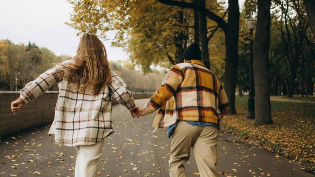 fall love, romance, Couple enjoying autumn day running through a park holding hands.