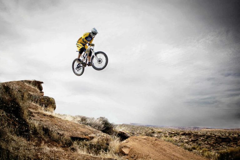 Challenge travel, adventure travel, A cyclist performs a daring jump off a rocky cliff under a cloudy sky.