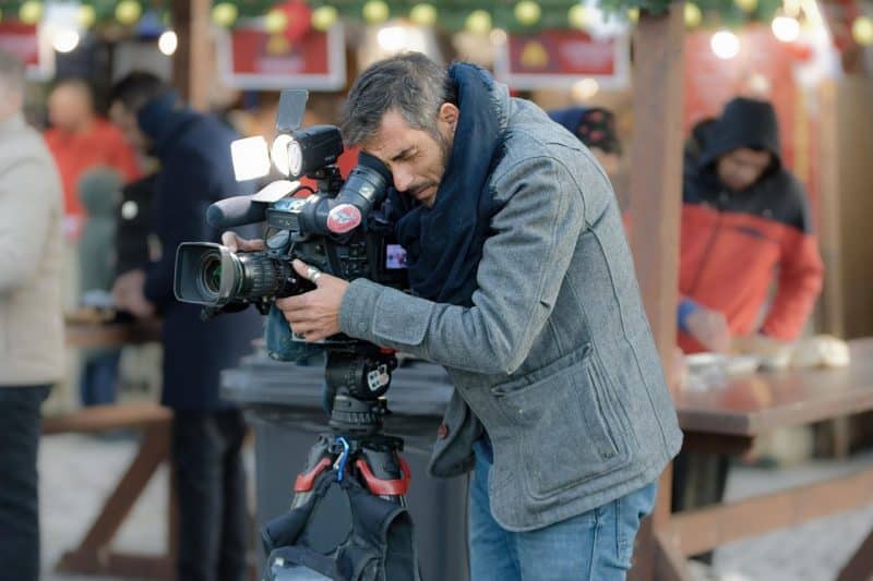 Cameraman recording a movie scene during the SCAD Savannah Film Festival Fest, surrounded by staff, equipment, and evening lights in a winter street photography setting.