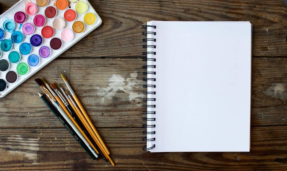 This photograph has a notebook, watercolor paints, and paint brushes. Creativity can be wonderful for brain health.