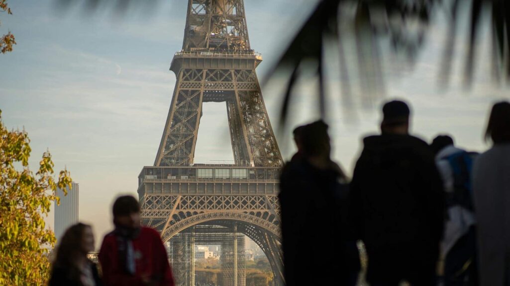 Tourists silhouette in front of Eiffel Tower, Paris landmark in soft daylight.