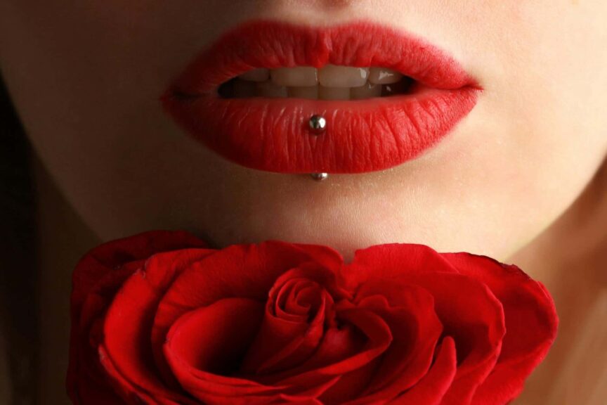 Aesthetic close-up featuring red lipstick, lip piercing, and a red rose. affordable makeup products