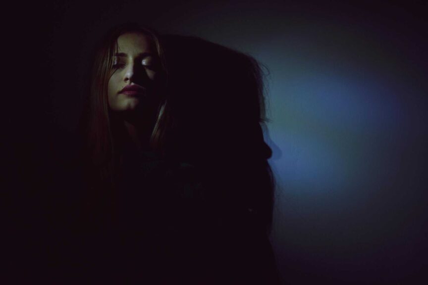 An artistic portrait of a woman with dark and moody lighting creating bold shadows. shadow work