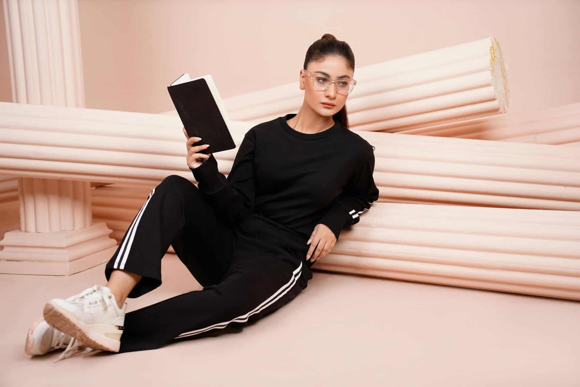 Woman in black athleisure holding a book against a classical column backdrop. Fall fashion, fashion trend