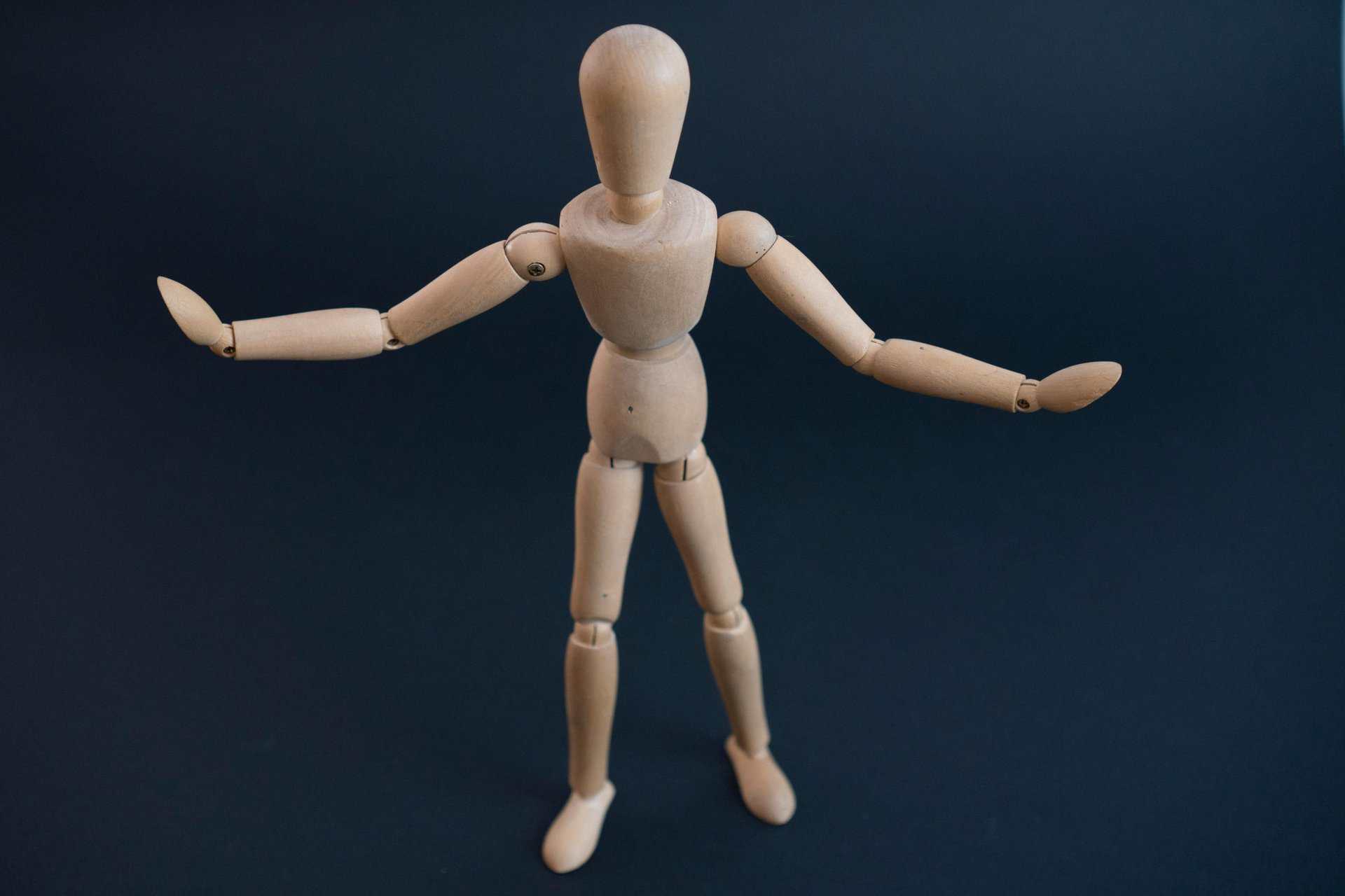 Close-up shot of a wooden art mannequin in a neutral pose on a dark background.