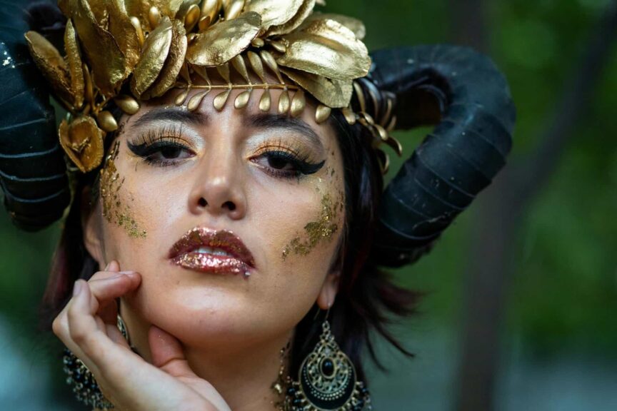 Elegant close-up portrait of a woman in fantasy costume with golden makeup and horns.