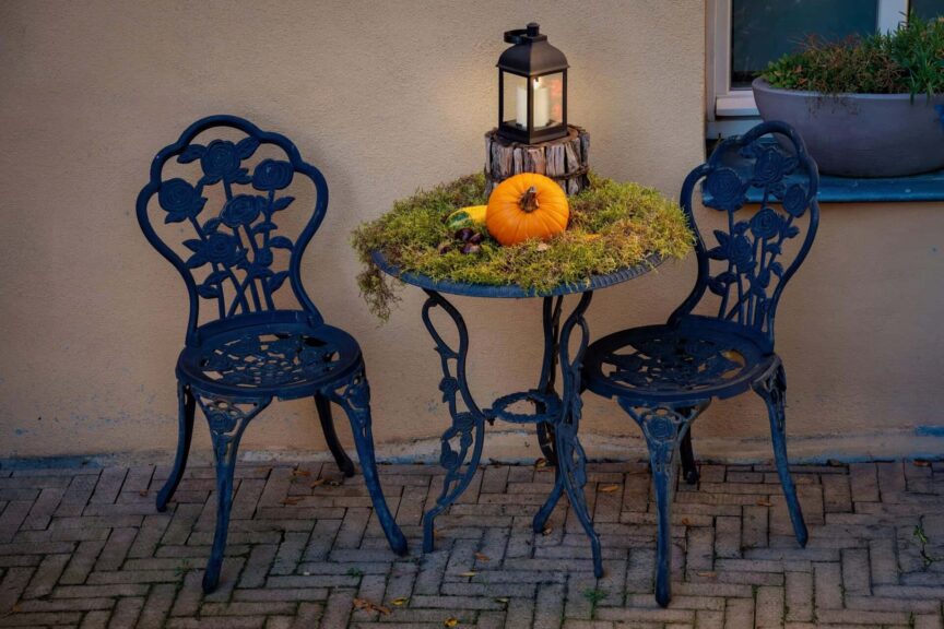 Charming outdoor fall setup with a pumpkin, lantern, and wrought iron furniture.