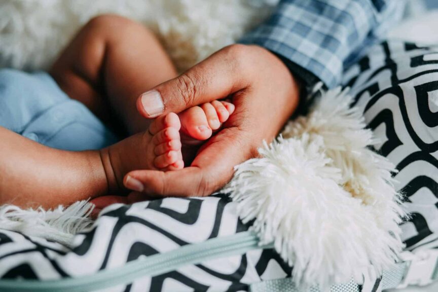 Close-up of an adult hand gently holding a baby's foot, symbolizing care and love. Paternal age, genetic mutation,
