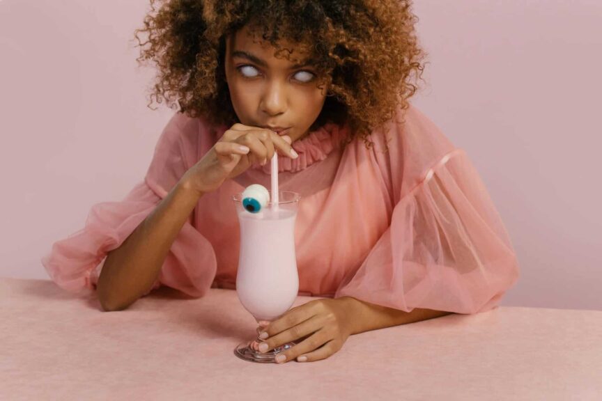 Young woman in a creative Halloween costume sipping a milkshake with a candy eyeball. halloween drinks