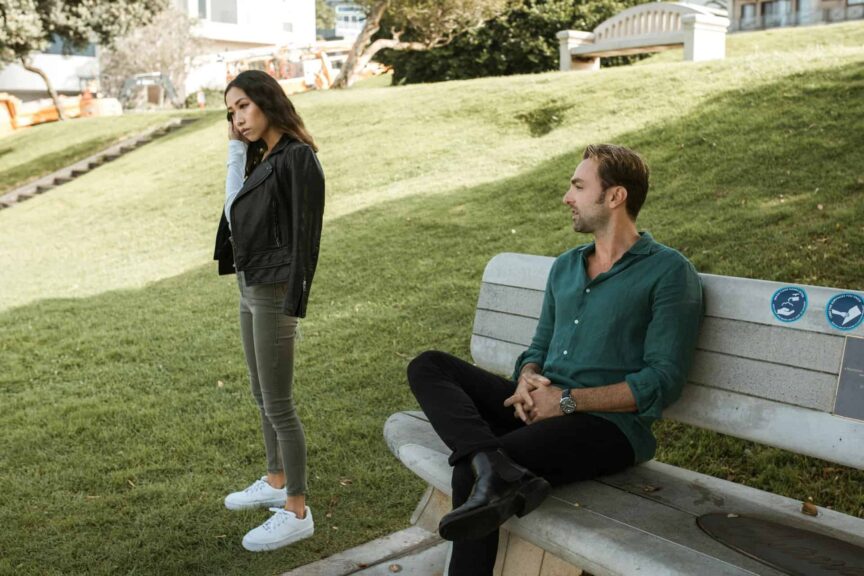 A couple having a disagreement on a park bench in a grassy outdoor setting. gaslighting