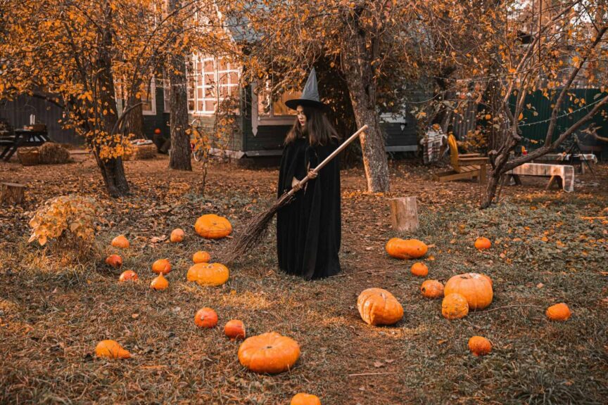 A witch in a classic costume stands among pumpkins in a fall-themed backyard, creating a perfect Halloween vibe of pure Autumn magic.