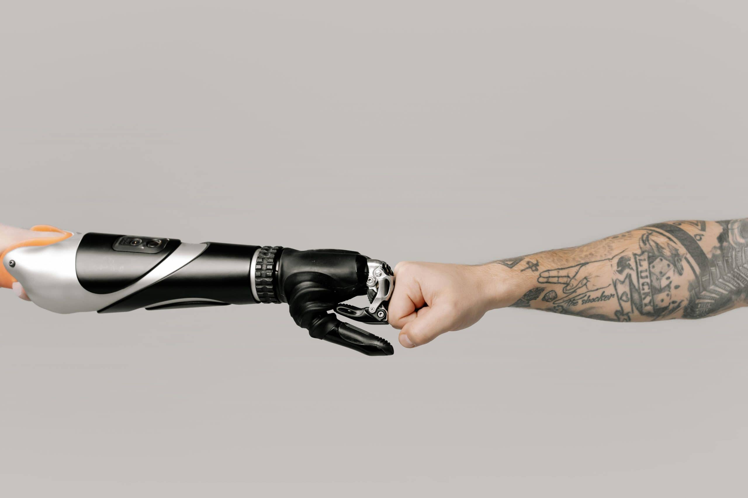 Close-up of a tattooed arm fist bumping with a robotic prosthetic arm in studio setting. Massage robots tom brady,