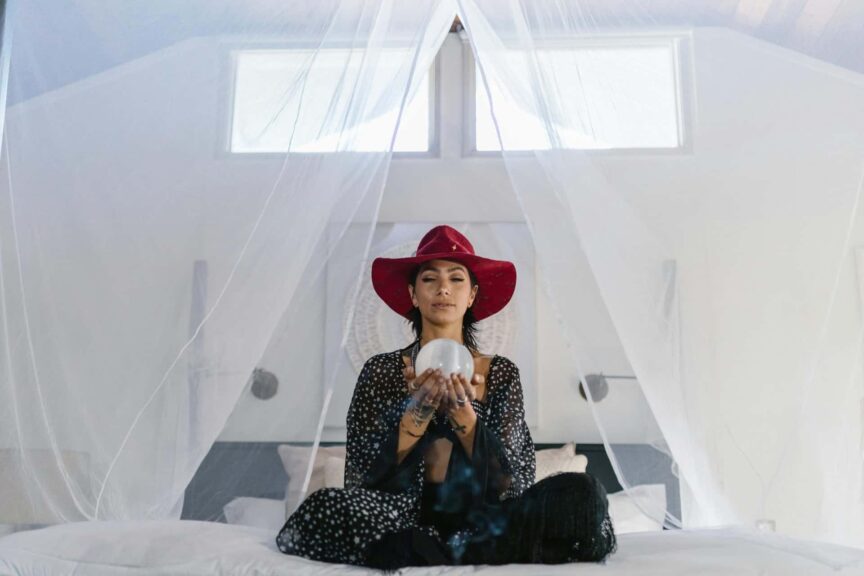 A woman wearing a red hat holds a crystal ball in an ethereal setting, suggesting mystery and magic. Intuitive list of zodiac signs.