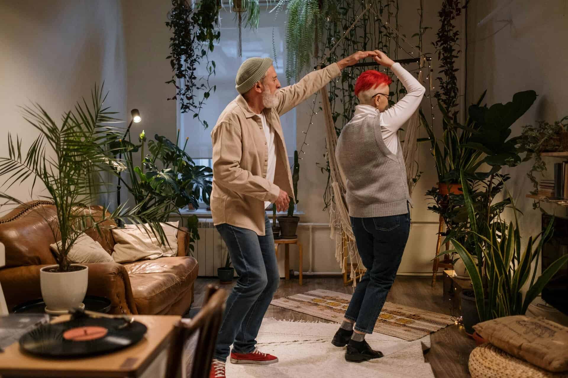 Joyful elderly couple dancing among houseplants in a cozy living room setting, embracing love and romance.