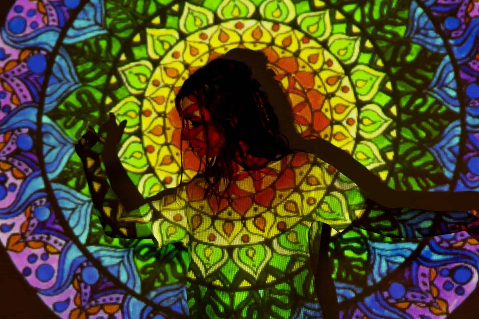 A vibrant mandala pattern projected onto a woman's silhouette, creating an artistic, esoteric atmosphere.