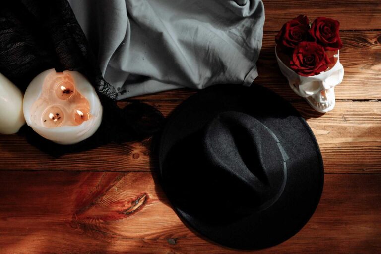 Flat lay image with black hat, skull, candles, and roses on wooden surface. Shadow work by zodiac sign.