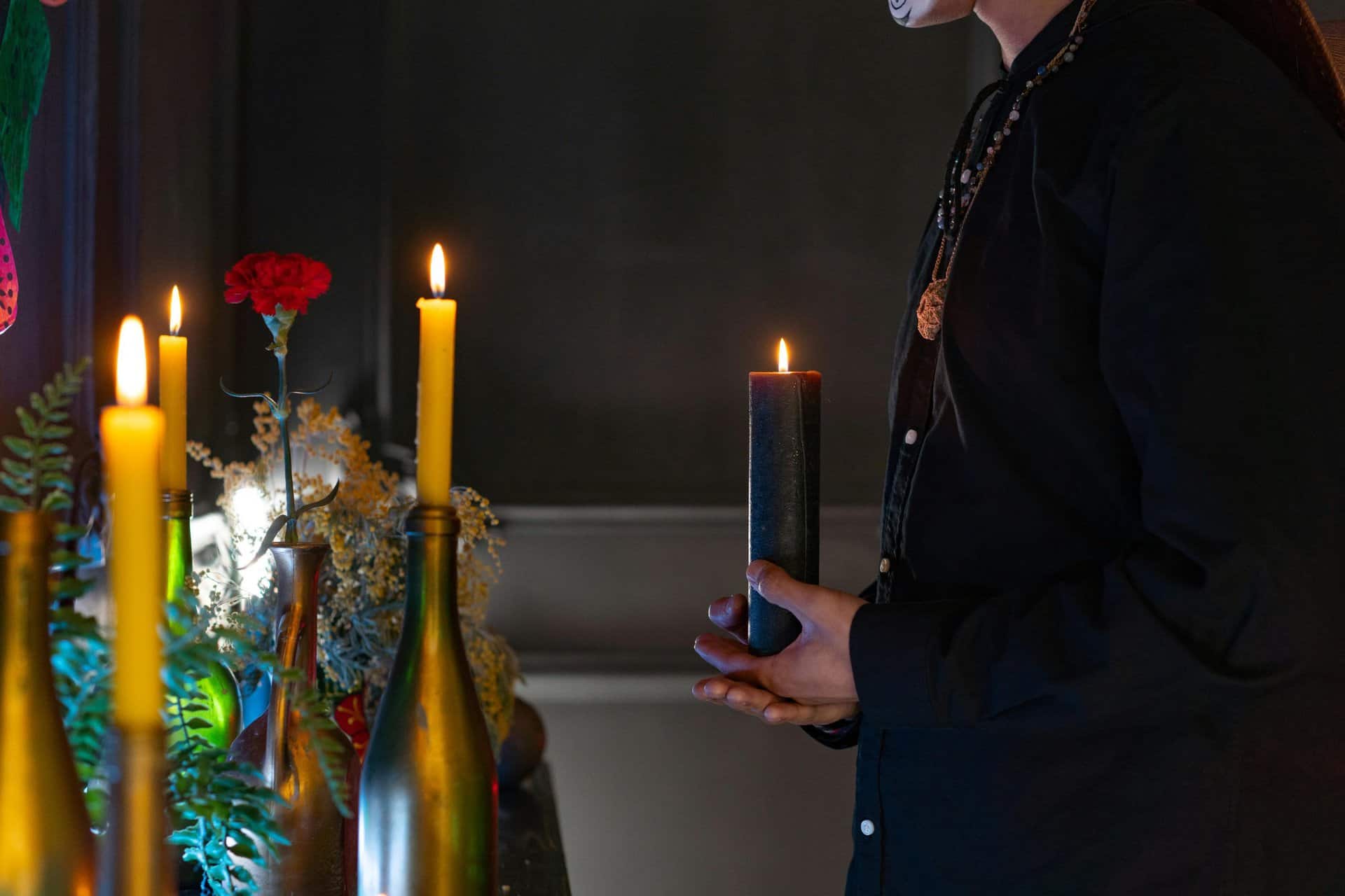 Close-up of an altar with candles, flowers, and a person in Day of the Dead makeup, creating a warm, spiritual ambiance. Sabbats