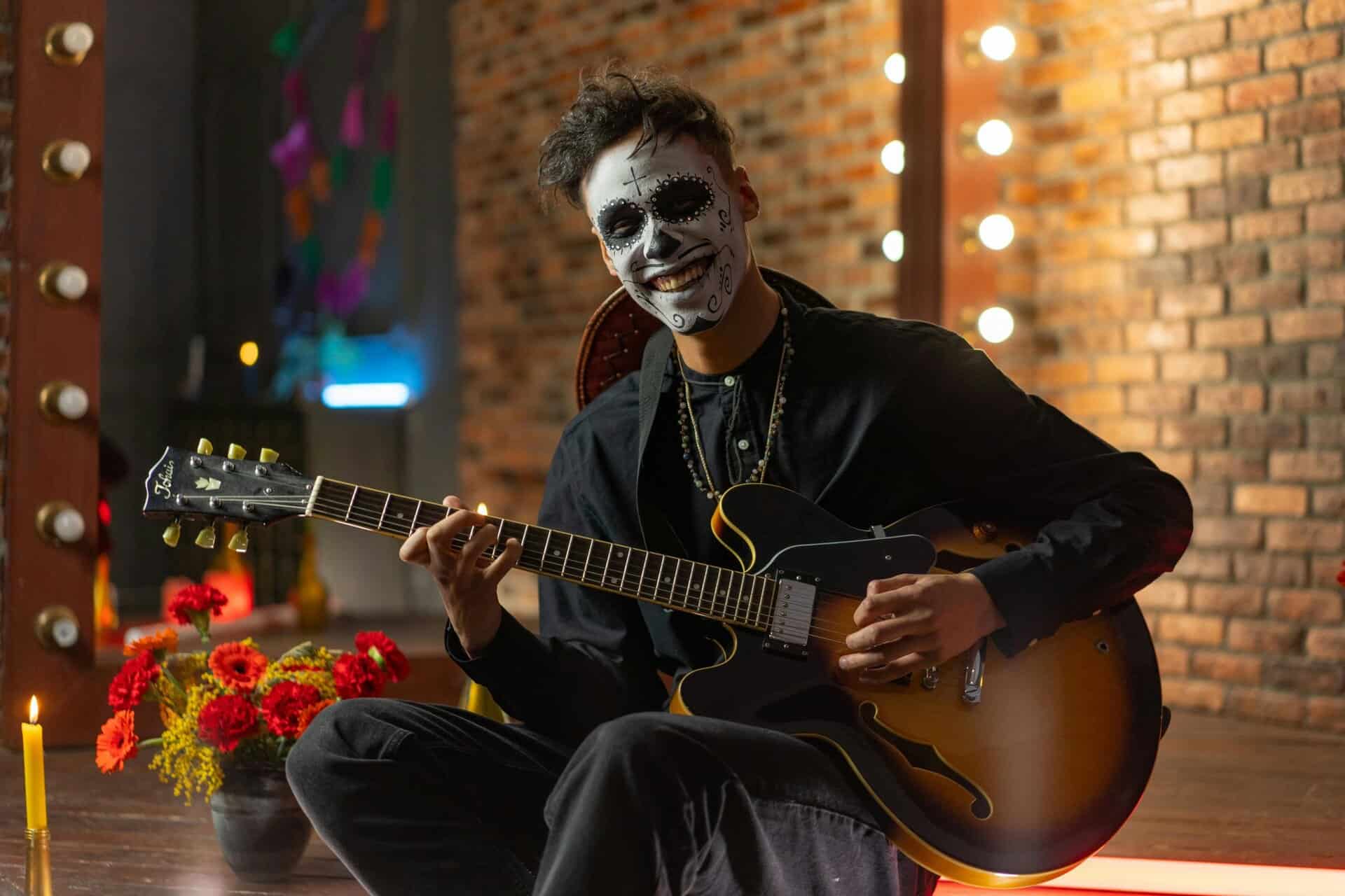 Musician with skeleton makeup plays guitar indoors, celebrating Day of the Dead.