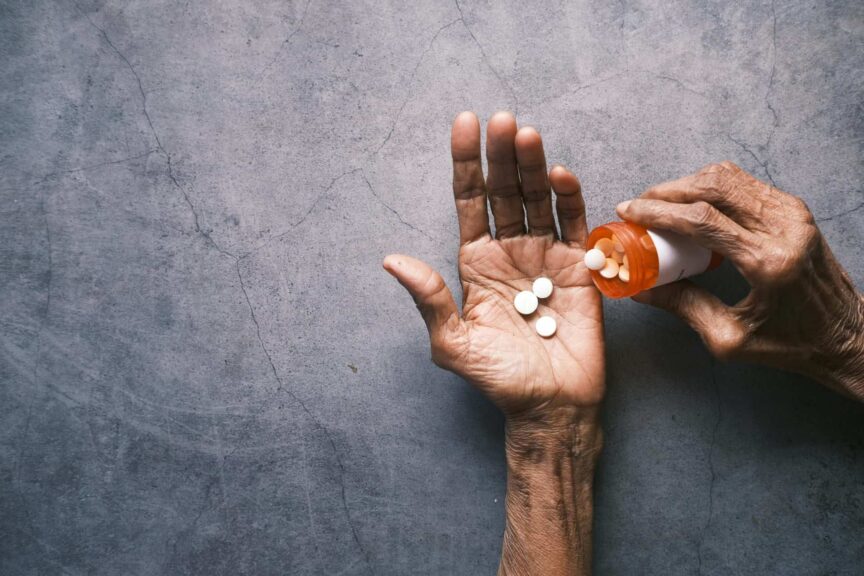 Elderly person's hand pouring pills from a bottle, offering ample copy space, slower aging.