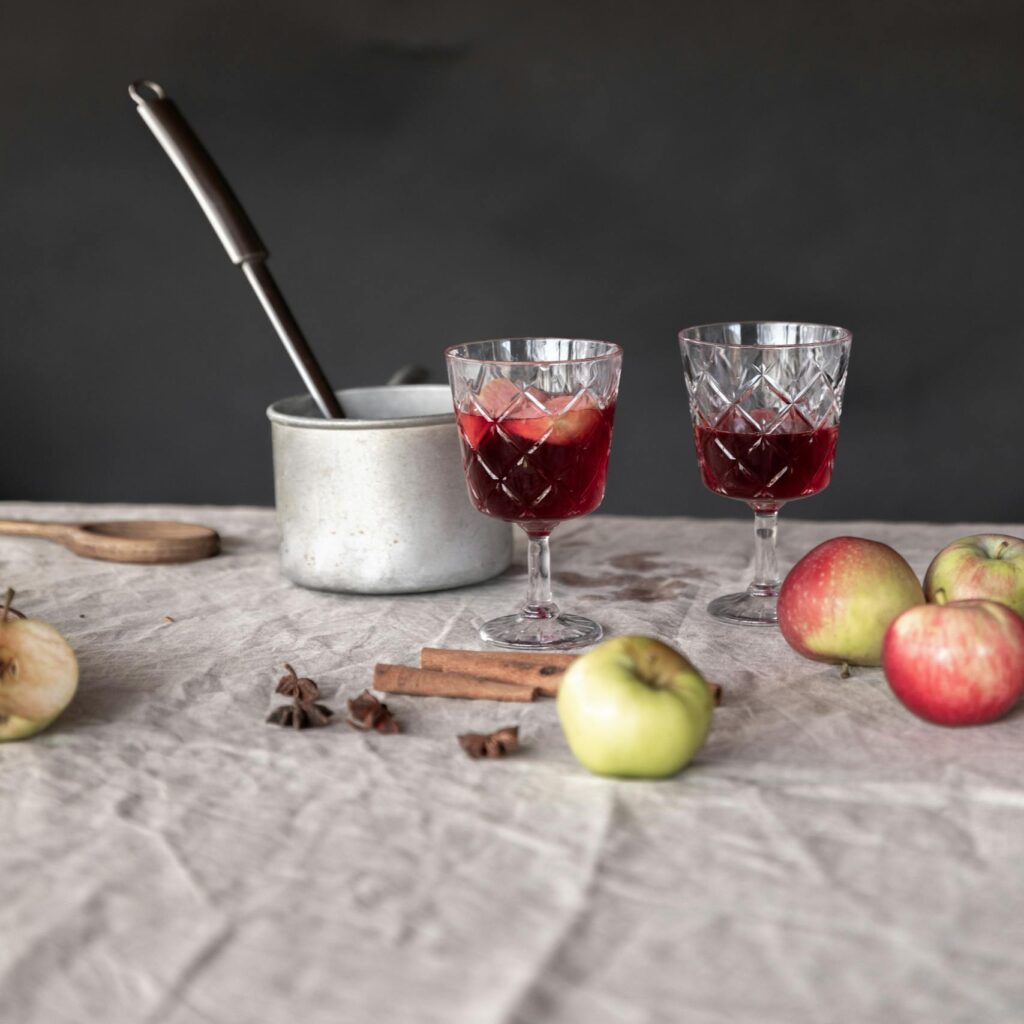 A cozy fall scene with two glasses of apple cinnamon mulled wine on a linen cloth with apples.