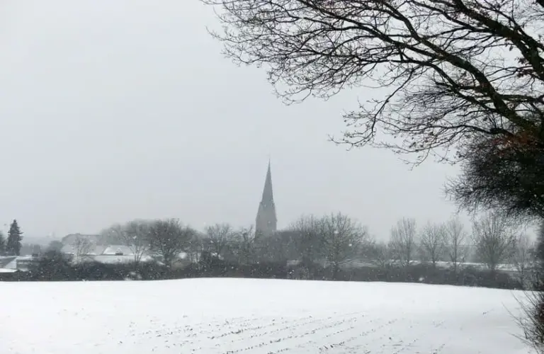 A snowy field with a church steeple in the distance. Solitude in winter.