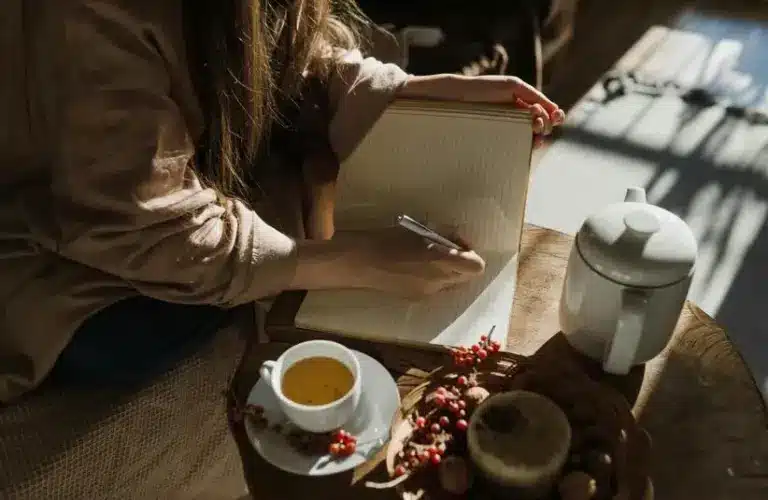 person journaling with a cup of tea in a cozy setting. Journaling prompts for fall