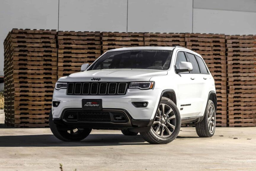 A sleek white Jeep Grand Cherokee parked in front of stacked wooden pallets, showcasing its luxury features.