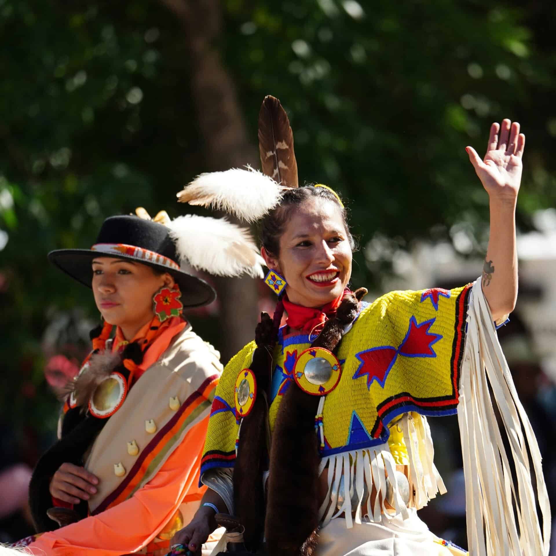 Smiling Native American women in vibrant traditional costumes celebrating outdoors.