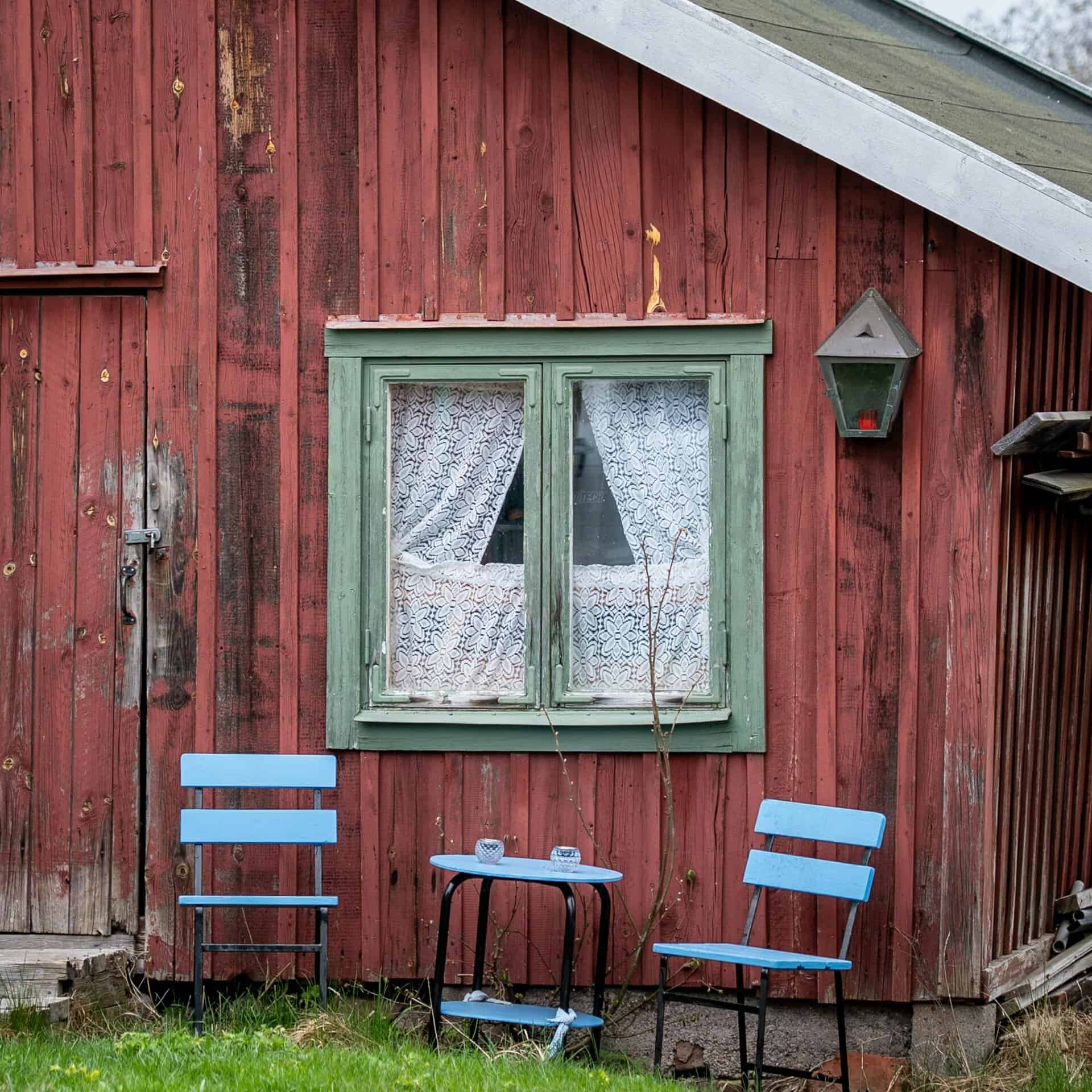 A vintage red wooden cabin with blue chairs and lace curtains in Vaxholm, Sweden.