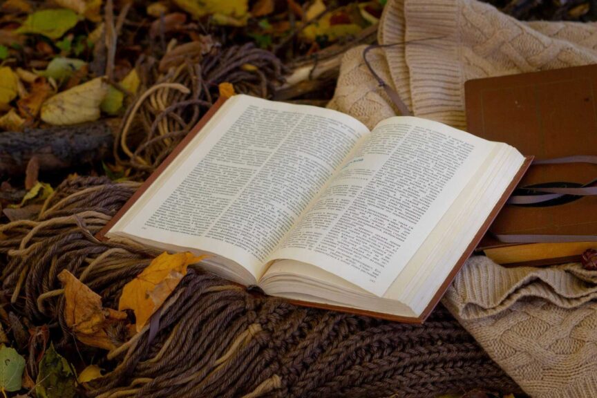 Open book on cozy knitted sweater surrounded by autumn leaves, perfect for seasonal reading vibes, daily devotion