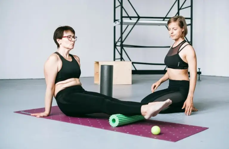 Two people sitting and exercising on a mat. Foam rolling for cold weather muscle recovery.