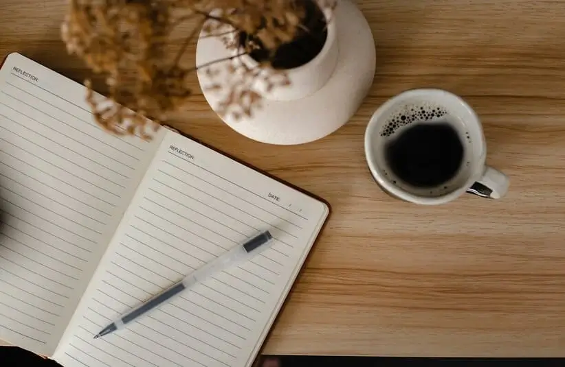 A journal or notebook, maybe a gratuity journal, cup of coffee, and flowers, on a desk. spiritual decluttering