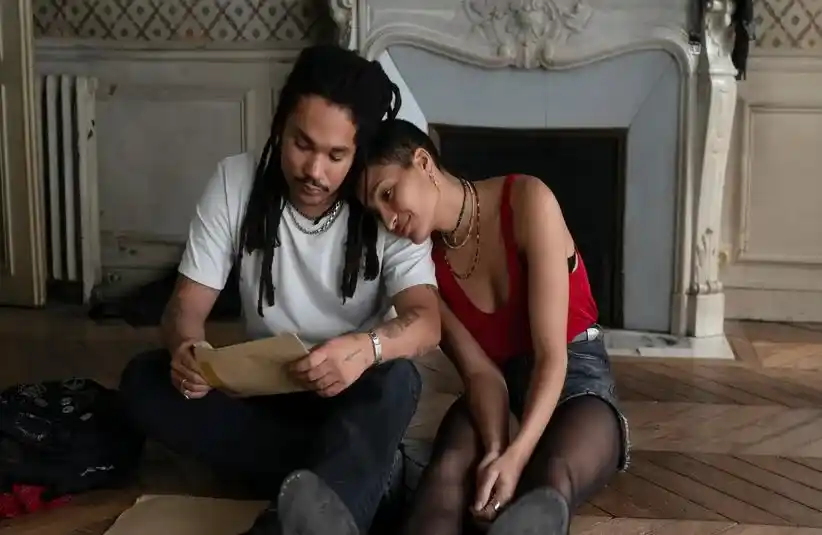 Indya Moore putting her head on Luka Sabbat's shoulder while opening an envelope.