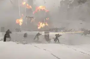 Helldivers 2 player characters in a snow-covered battlefield with five soldiers firing weapons amidst explosions. Bright orange blasts illuminate the snowy terrain, creating a tense atmosphere.