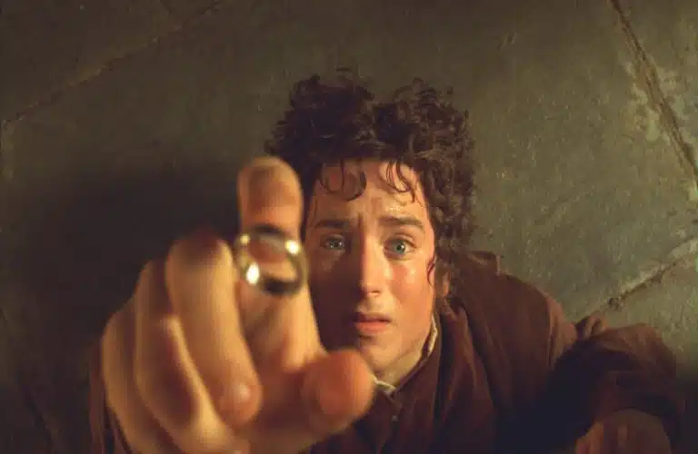 Frodo Baggins, from "The Lord of the Rings: The Fellowship of the Ring," reaches toward a hovering gold ring with a determined expression. The scene conveys tension and focus. Stone floor background.