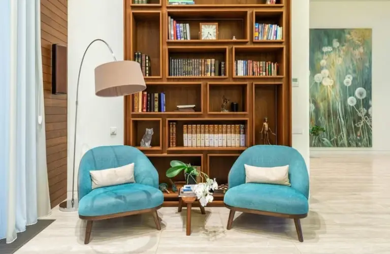 A reading nook with a floor lamp, 2 chairs, a small table, and a bookshelf behind