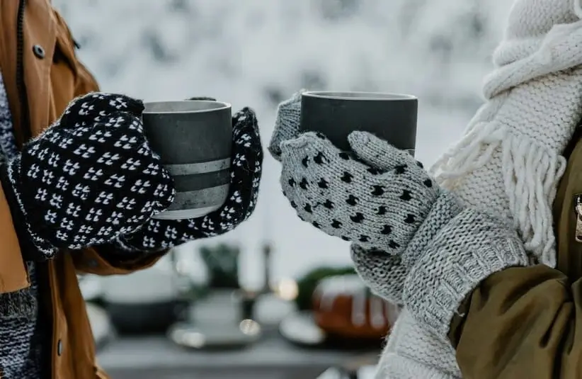 Two people wearing mittens and holding mugs