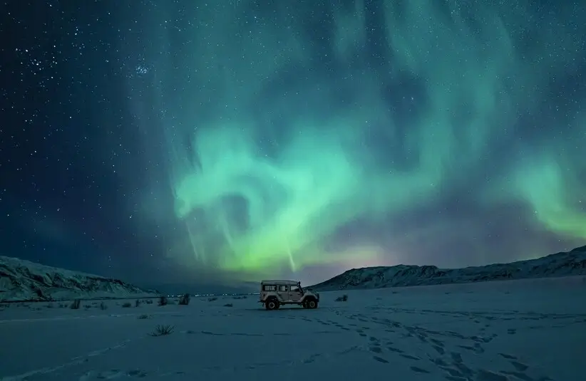 SUV on snow with the northern lights (aurora borealis) behind it