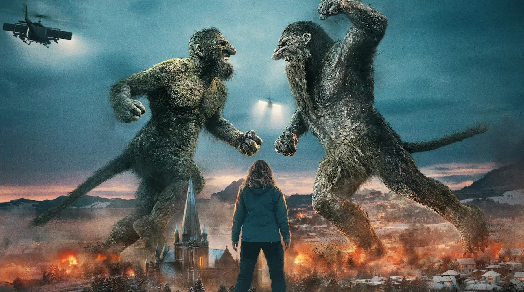 A person stands facing two giant trolls battling above a fiery village, with a helicopter nearby. The scene conveys tension and epic conflict.