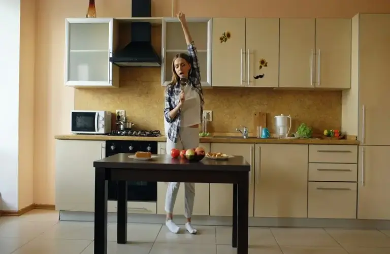 Cheerful young funny woman dancing and singing with ladle while while cooking in the kitchen at home in the morning, holiday