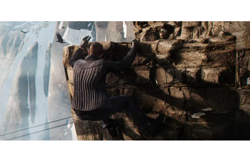 Man in a gray jacket climbs a rugged, rocky cliff. Snowy peaks and birds create an adventurous, tense atmosphere. 007 First Light, Courtesy of IO Interactive A/S