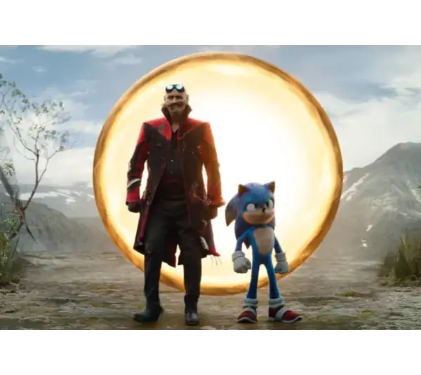 A blue anthropomorphic hedgehog and a man in a black and red coat stand on a dirt road near a glowing golden ring. Mountains and cloudy sky are in the background. Dr. Robotnik (portrayed by Jim Carrey) and Sonic,(portrayed by Ben Schwarz) Courtesy of Paramount Pictures and Sega of America, Inc.