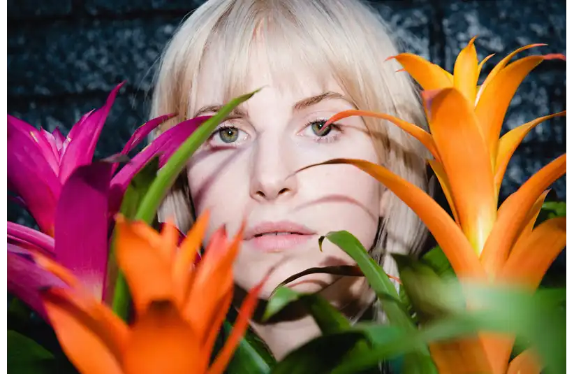 Photo of singer Hayley Williams peeking through some colorful plants.