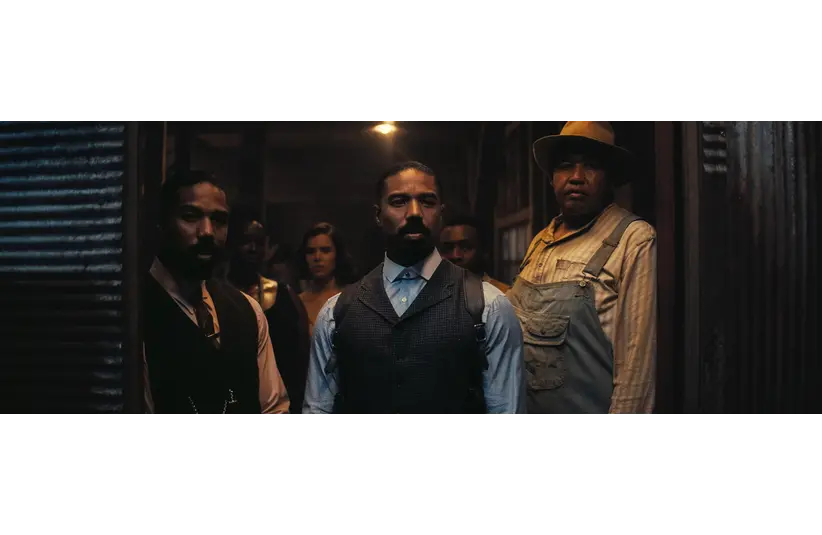 A group of serious-looking people, dressed in period clothing, stand in a dimly lit room. They gaze intently at something outside the frame, conveying tension.