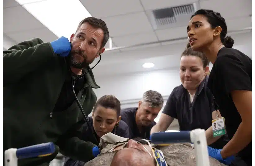 A team of medical professionals, including a man with a stethoscope and a woman with a doctor badge, gather around a patient in an emergency setting, focused and concerned.